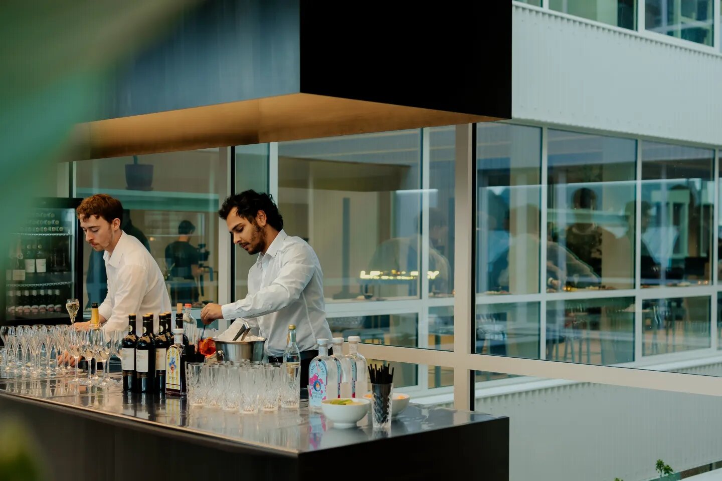 Twee Beyond the Serve-medewerkers in wit hemd schenken drankjes aan een bar tijdens een event